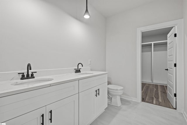 full bath featuring toilet, double vanity, baseboards, and a sink