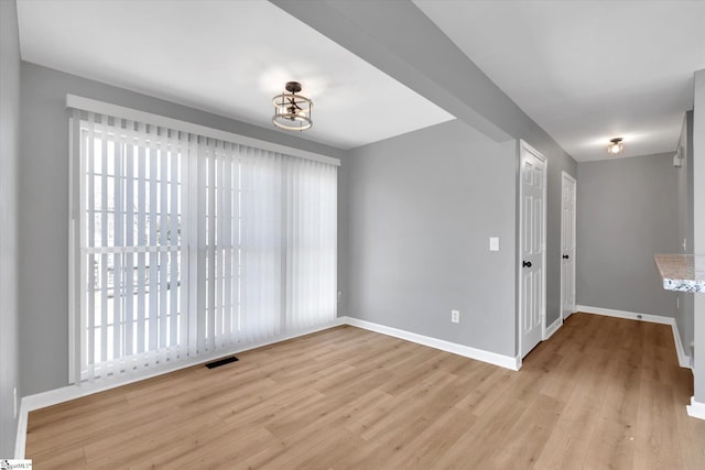 unfurnished room featuring light wood-style flooring, visible vents, and baseboards