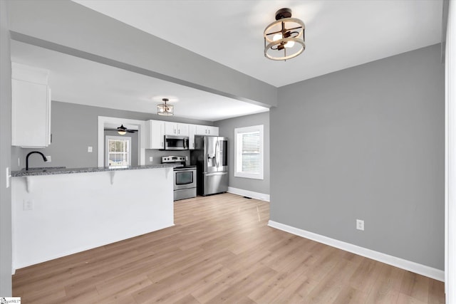 kitchen featuring light wood-style flooring, appliances with stainless steel finishes, white cabinets, dark stone counters, and a kitchen breakfast bar