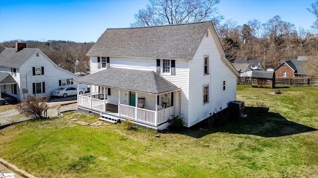 back of house with a porch, roof with shingles, and a lawn