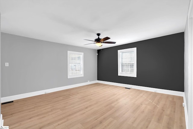 unfurnished room with a healthy amount of sunlight, light wood-type flooring, visible vents, and baseboards