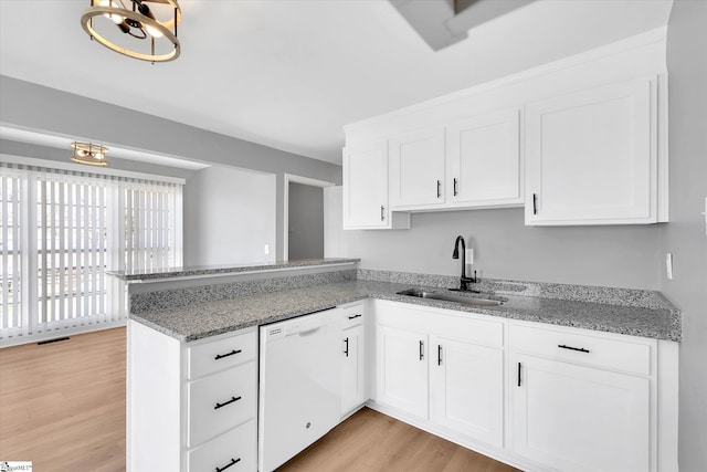 kitchen featuring white cabinets, dishwasher, light wood-style flooring, a peninsula, and a sink