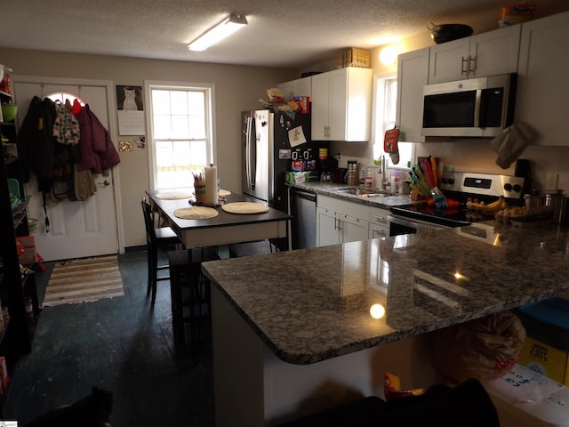 kitchen featuring a textured ceiling, appliances with stainless steel finishes, dark stone countertops, and a sink