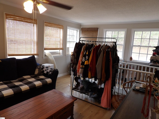 living area with a textured ceiling, ornamental molding, wood finished floors, and baseboards