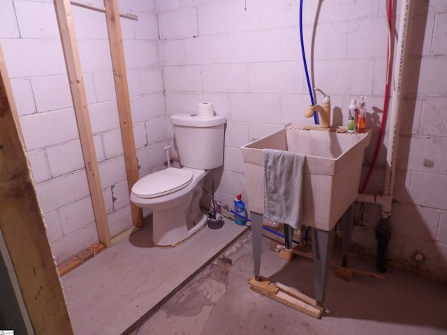 bathroom with toilet, concrete flooring, and concrete block wall