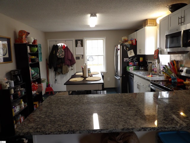 kitchen with stainless steel appliances, stone countertops, white cabinets, and a textured ceiling