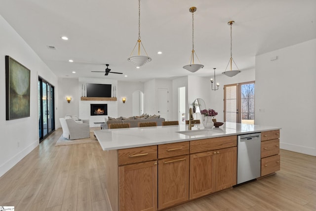 kitchen featuring light wood finished floors, dishwasher, open floor plan, a fireplace, and a sink