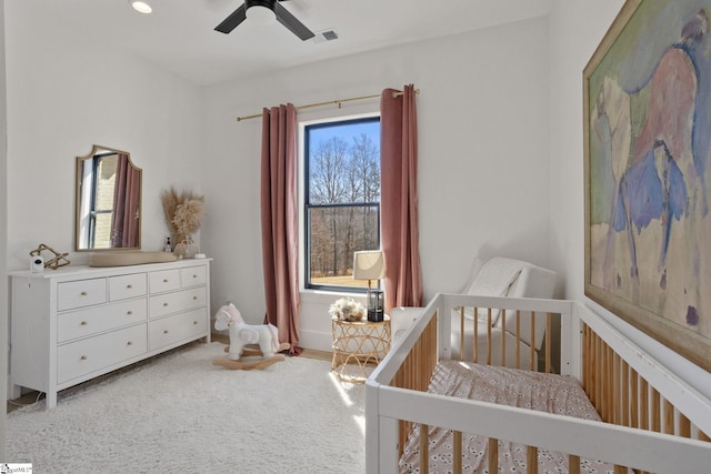 carpeted bedroom featuring a crib, visible vents, and a ceiling fan