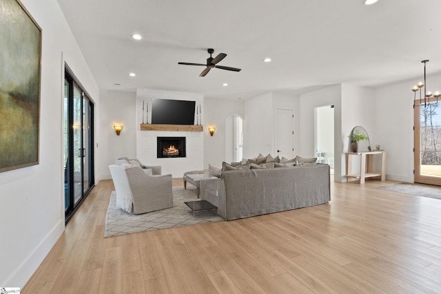 living room featuring a fireplace, recessed lighting, light wood-style floors, baseboards, and ceiling fan with notable chandelier