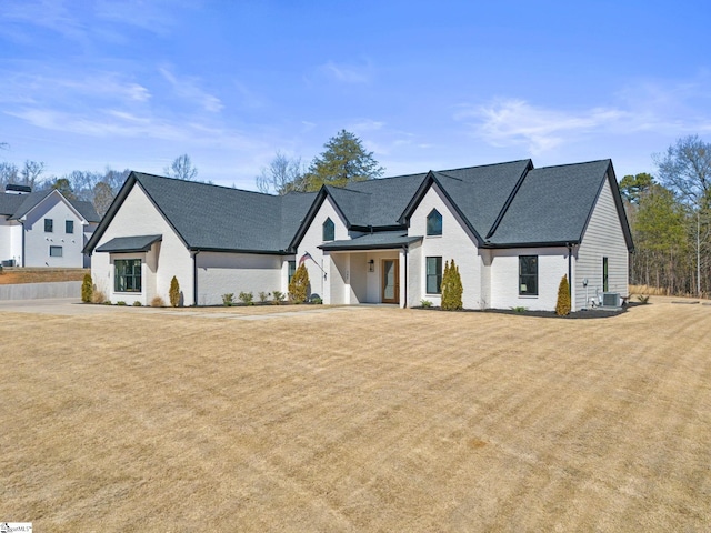 modern farmhouse featuring brick siding, a front lawn, and central air condition unit