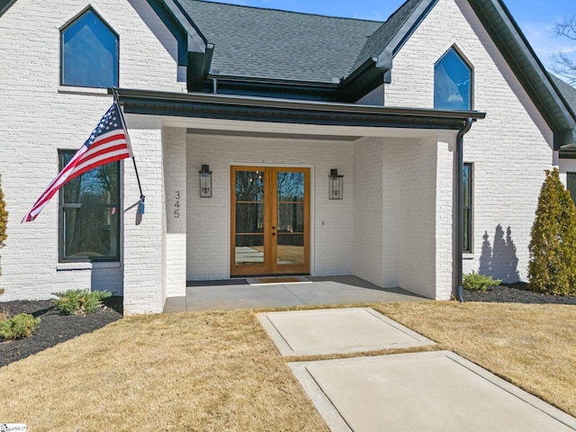 property entrance featuring a shingled roof, french doors, and brick siding