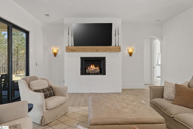 living area featuring arched walkways, a brick fireplace, visible vents, and wood finished floors