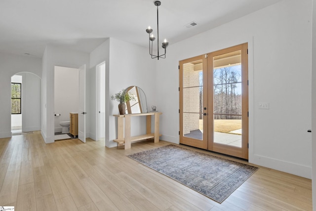 doorway to outside featuring arched walkways, french doors, visible vents, light wood-style flooring, and baseboards