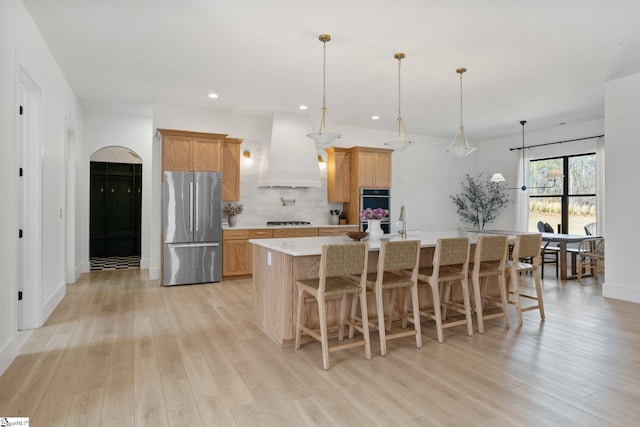 kitchen featuring light wood finished floors, custom range hood, appliances with stainless steel finishes, and light countertops