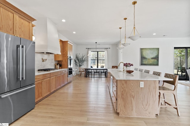 kitchen with stainless steel appliances, light countertops, light wood-style flooring, decorative backsplash, and premium range hood