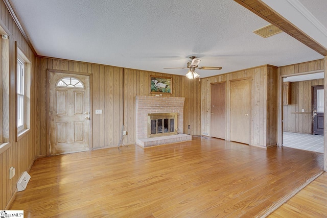 unfurnished living room featuring visible vents, light wood-style flooring, a ceiling fan, a brick fireplace, and a textured ceiling