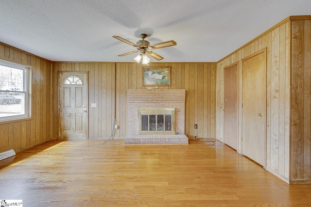 unfurnished living room featuring a brick fireplace, wood walls, a textured ceiling, and wood finished floors