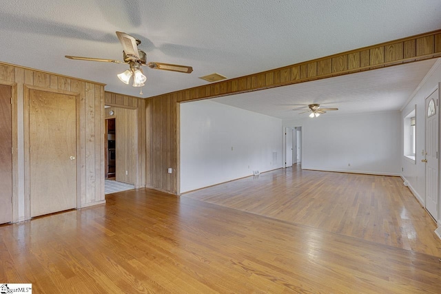 empty room with ceiling fan, wood walls, and wood finished floors