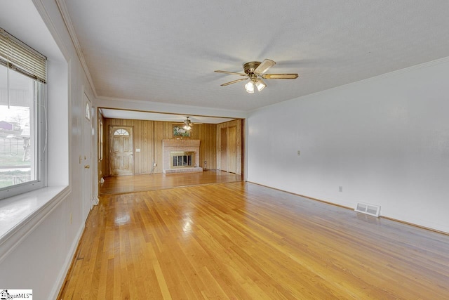 unfurnished living room featuring a fireplace, crown molding, visible vents, light wood-style floors, and ceiling fan