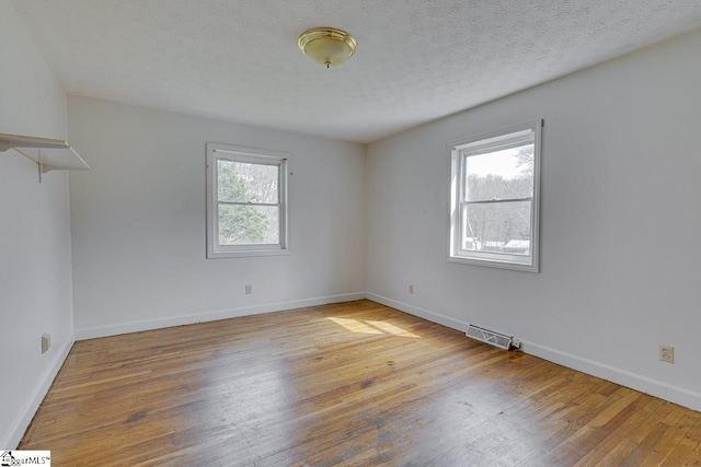 empty room featuring visible vents, a textured ceiling, baseboards, and wood finished floors