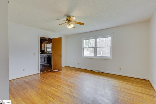 empty room featuring visible vents, baseboards, ceiling fan, a textured ceiling, and light wood-style floors