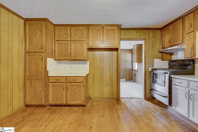 kitchen featuring brown cabinets, under cabinet range hood, light countertops, light wood-type flooring, and stainless steel range with electric stovetop