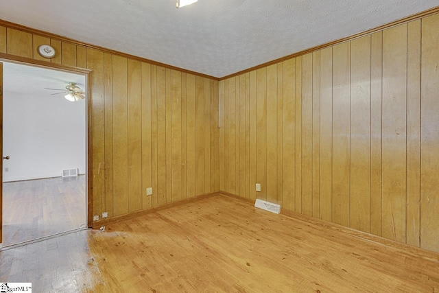 spare room with wood-type flooring, visible vents, ceiling fan, and wood walls