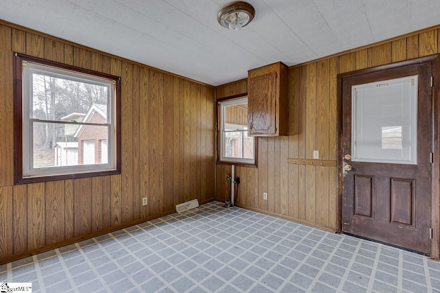 empty room with light floors, visible vents, wood walls, and baseboards