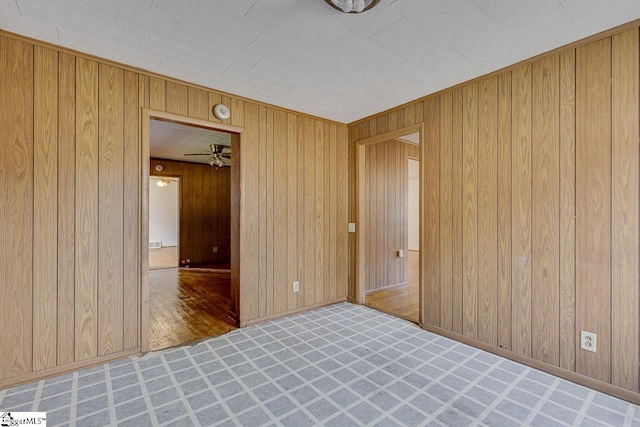 empty room with wood walls, ceiling fan, and baseboards