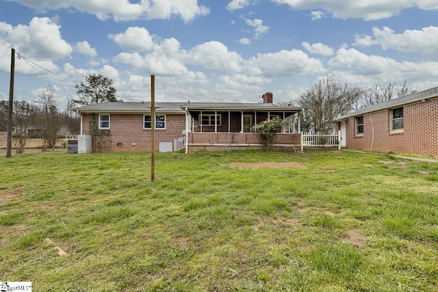 back of house featuring a chimney, crawl space, covered porch, a yard, and brick siding