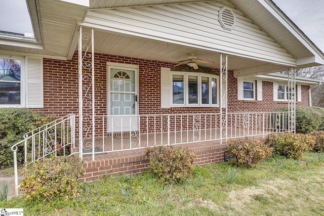 view of exterior entry with ceiling fan, a porch, and brick siding