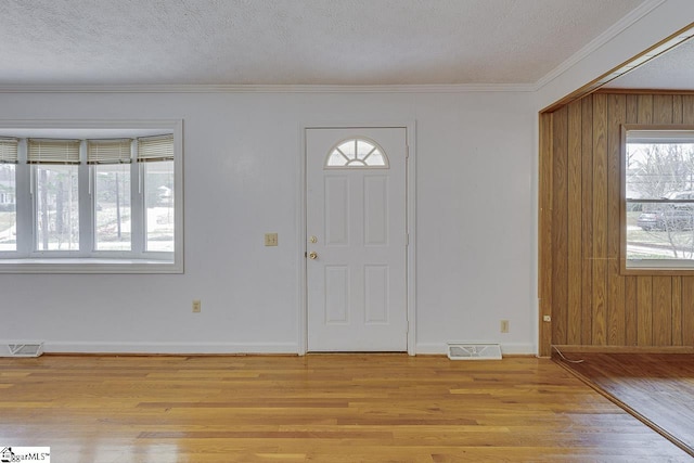 entrance foyer featuring light wood-type flooring, a textured ceiling, visible vents, and crown molding