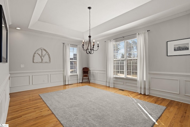 unfurnished dining area featuring light wood-style flooring, crown molding, a tray ceiling, and a notable chandelier