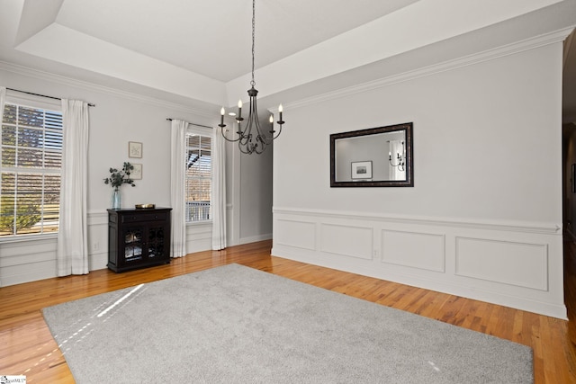 unfurnished dining area with an inviting chandelier, a tray ceiling, a wealth of natural light, and wood finished floors