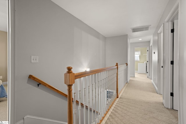 hallway featuring carpet flooring, visible vents, baseboards, and an upstairs landing