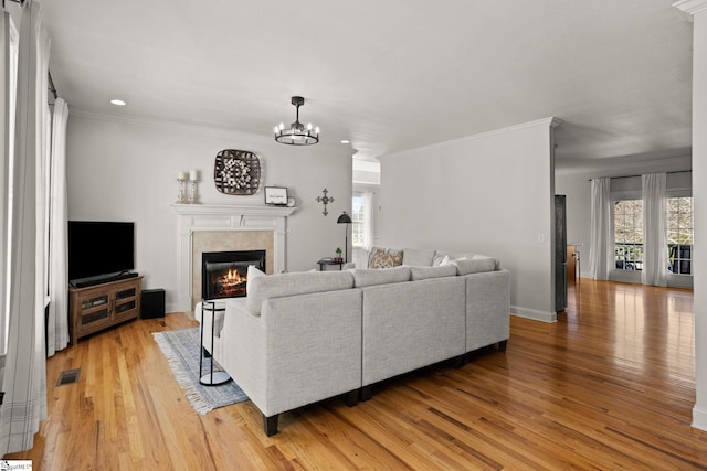 living room featuring light wood-type flooring, a glass covered fireplace, visible vents, and a notable chandelier