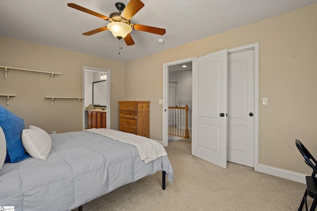 bedroom featuring light carpet, ceiling fan, ensuite bath, and baseboards