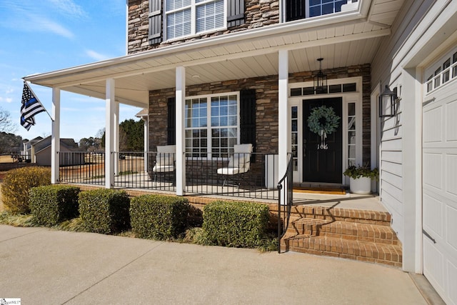 entrance to property with a porch, stone siding, and a garage