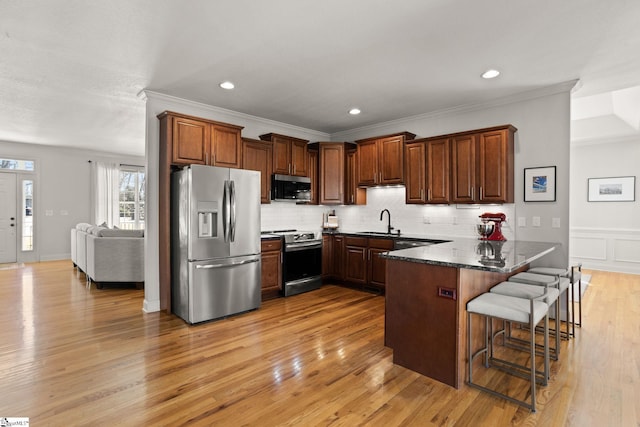 kitchen featuring appliances with stainless steel finishes, a breakfast bar, a peninsula, a sink, and backsplash