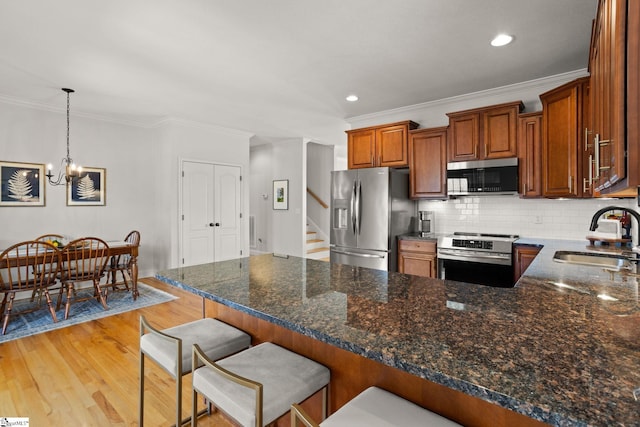 kitchen featuring a peninsula, a sink, stainless steel appliances, light wood-type flooring, and backsplash