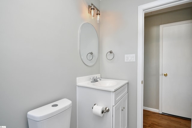 half bathroom with toilet, wood finished floors, and vanity