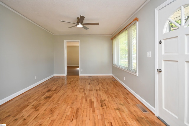 empty room featuring ornamental molding, light wood-type flooring, visible vents, and baseboards