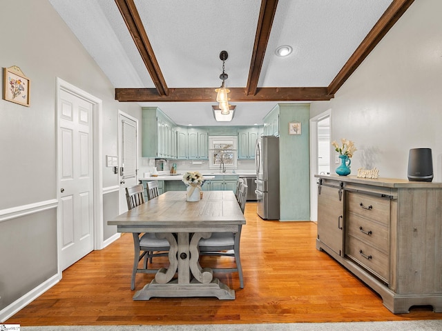 dining space with a textured ceiling, light wood-type flooring, beam ceiling, and baseboards