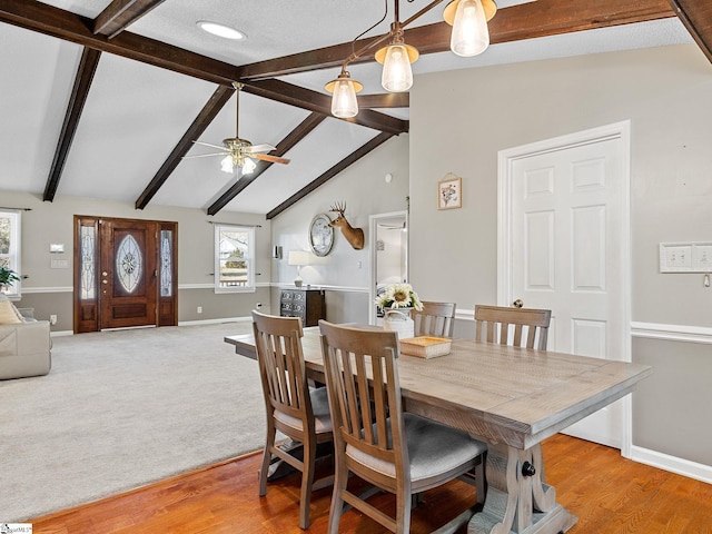 dining area with lofted ceiling with beams, light wood-type flooring, light carpet, and baseboards