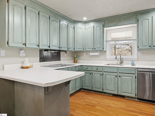 kitchen featuring a peninsula, black electric cooktop, stainless steel dishwasher, light wood-style floors, and a sink