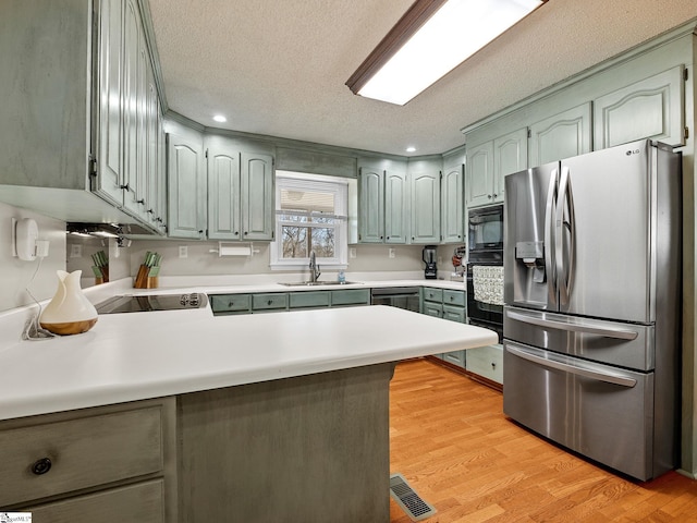 kitchen with visible vents, light wood-style flooring, a sink, a peninsula, and black appliances