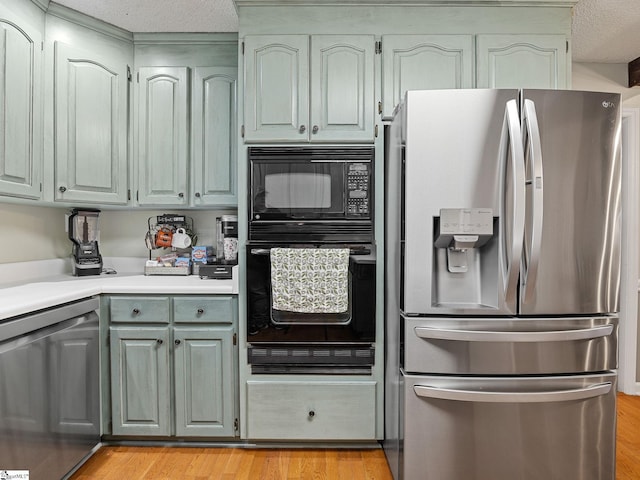 kitchen featuring a textured ceiling, light wood-style flooring, light countertops, gray cabinets, and black appliances