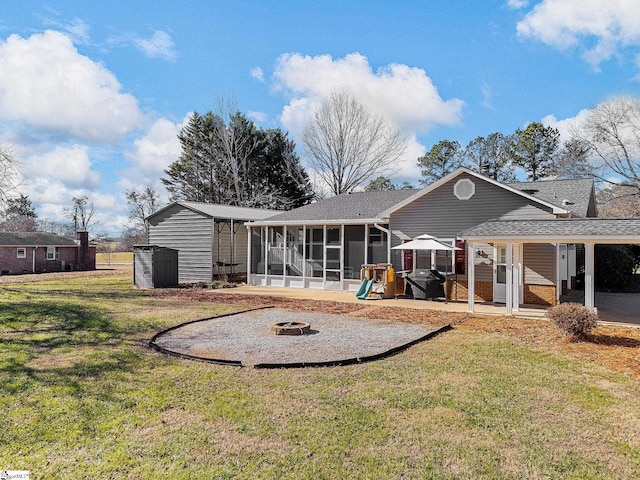 back of house featuring an outbuilding, a patio, a lawn, an outdoor fire pit, and a sunroom