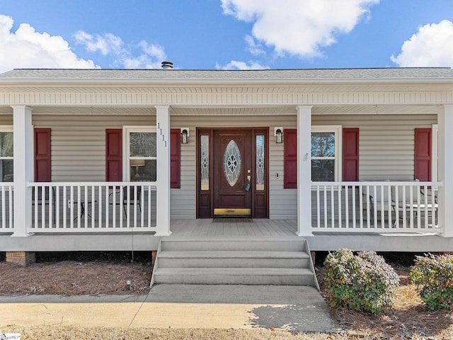 doorway to property featuring a porch and a shingled roof