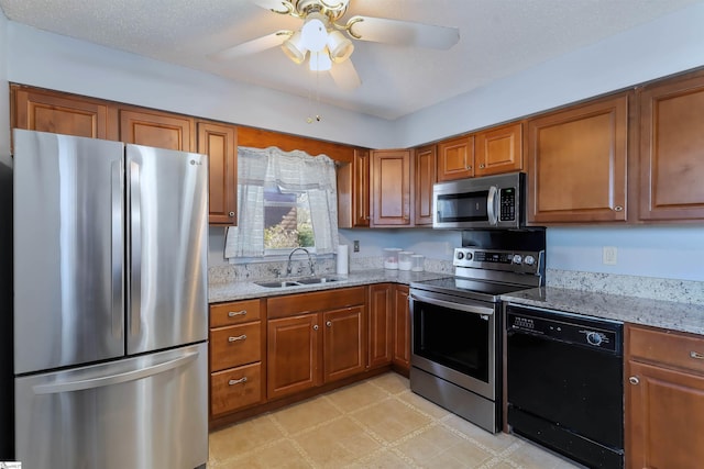 kitchen with stainless steel appliances, light stone counters, a sink, and brown cabinets